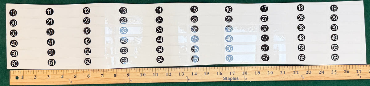 Clear vinyl sheet of dry-erase slot number price stickers, slots 10 to 69, next to a yardstick